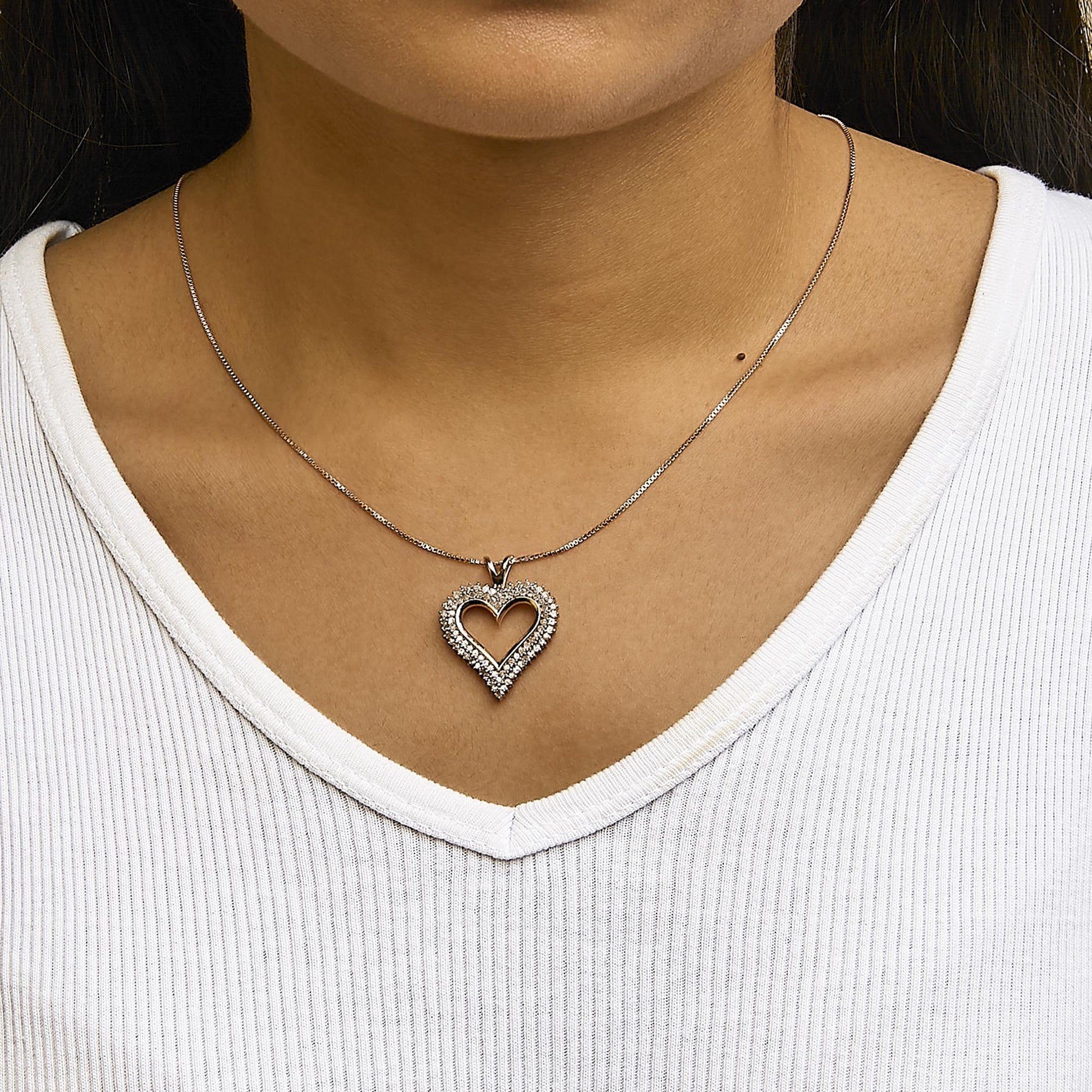Close-up front view of a rose-colored heart-shaped necklace pendant with white round gemstones in prong settings, worn on a model.