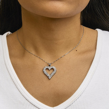 Close-up front view of a white metal necklace with a heart-shaped open pendant adorned with round white gemstones, worn on a model.