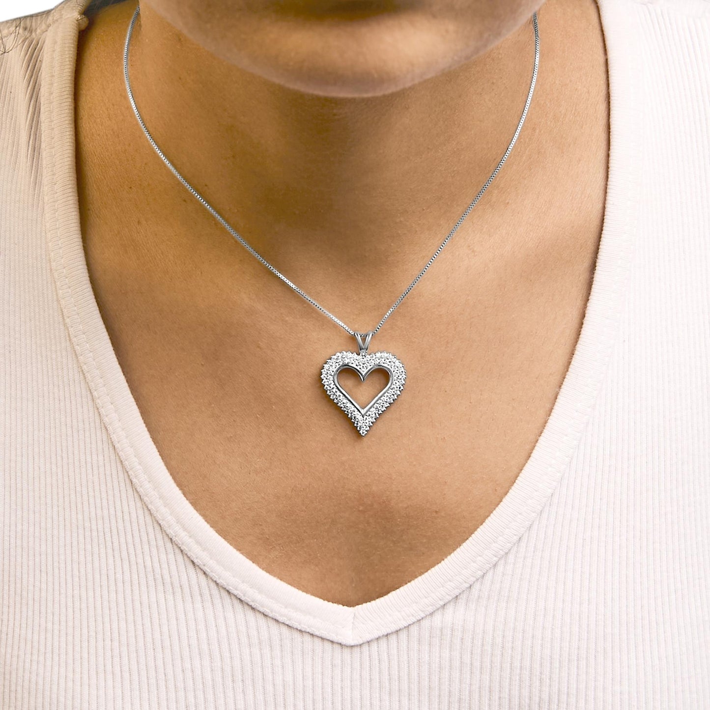 Close-up front view of a white metal necklace with a heart-shaped pendant adorned with small round white gemstones worn on a model.