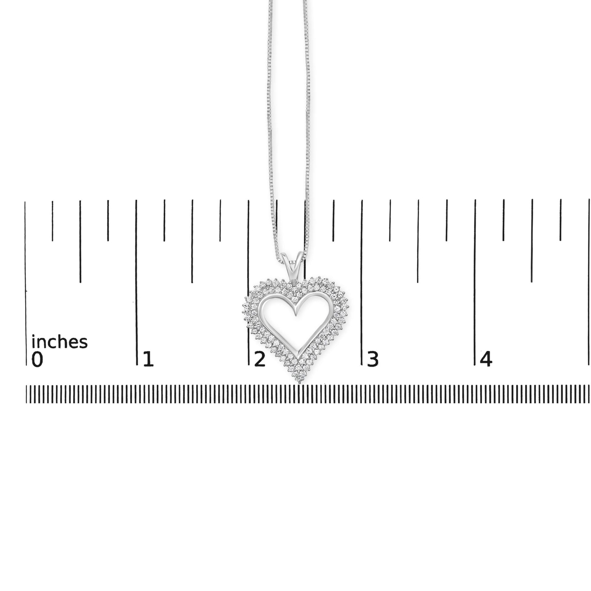 Heart-shaped white metal necklace pendant with round white gemstones in shared prong setting, shown hanging above a ruler for size reference, front view.