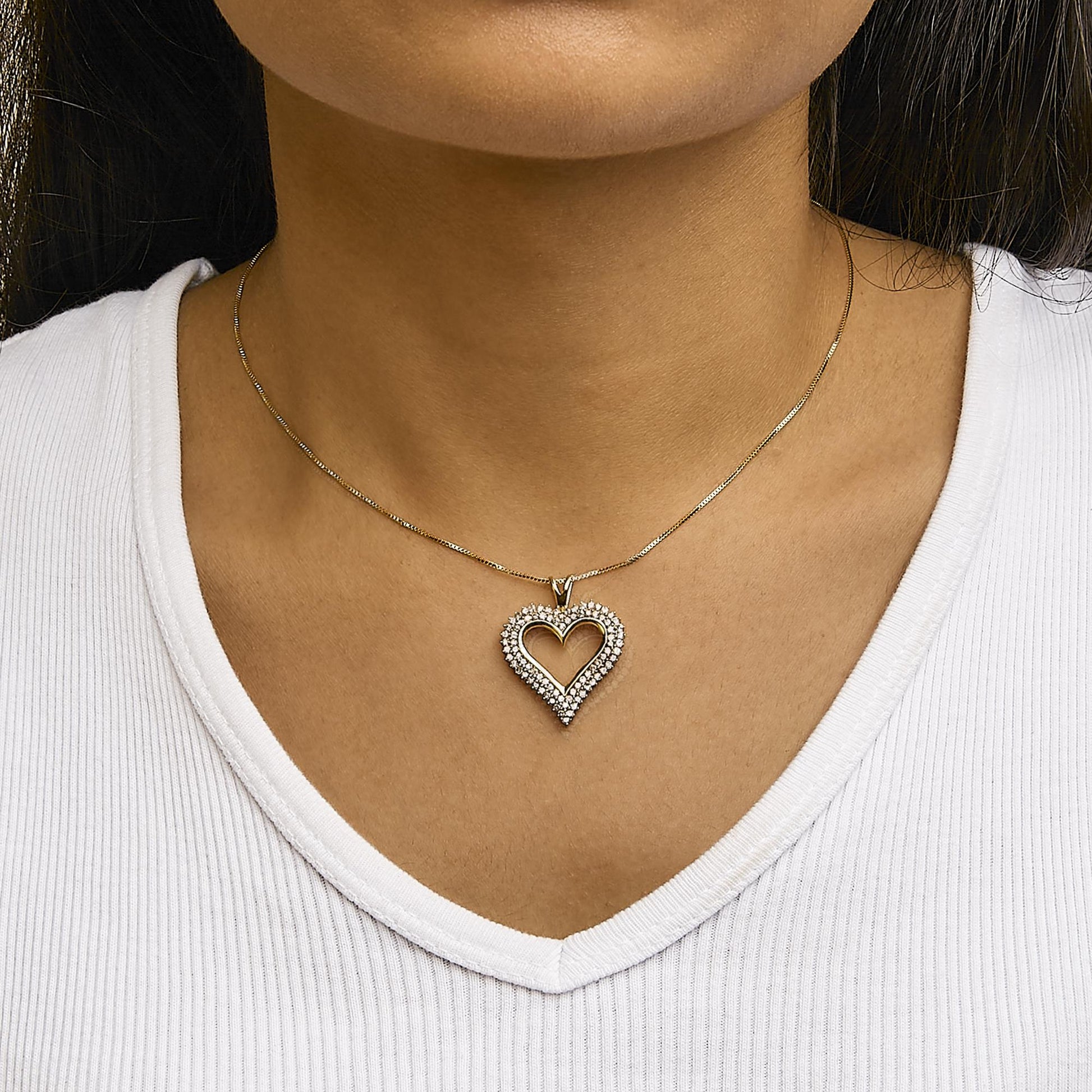 Front view of a yellow metal heart-shaped necklace pendant with white round prong-set gemstones, worn on a model.