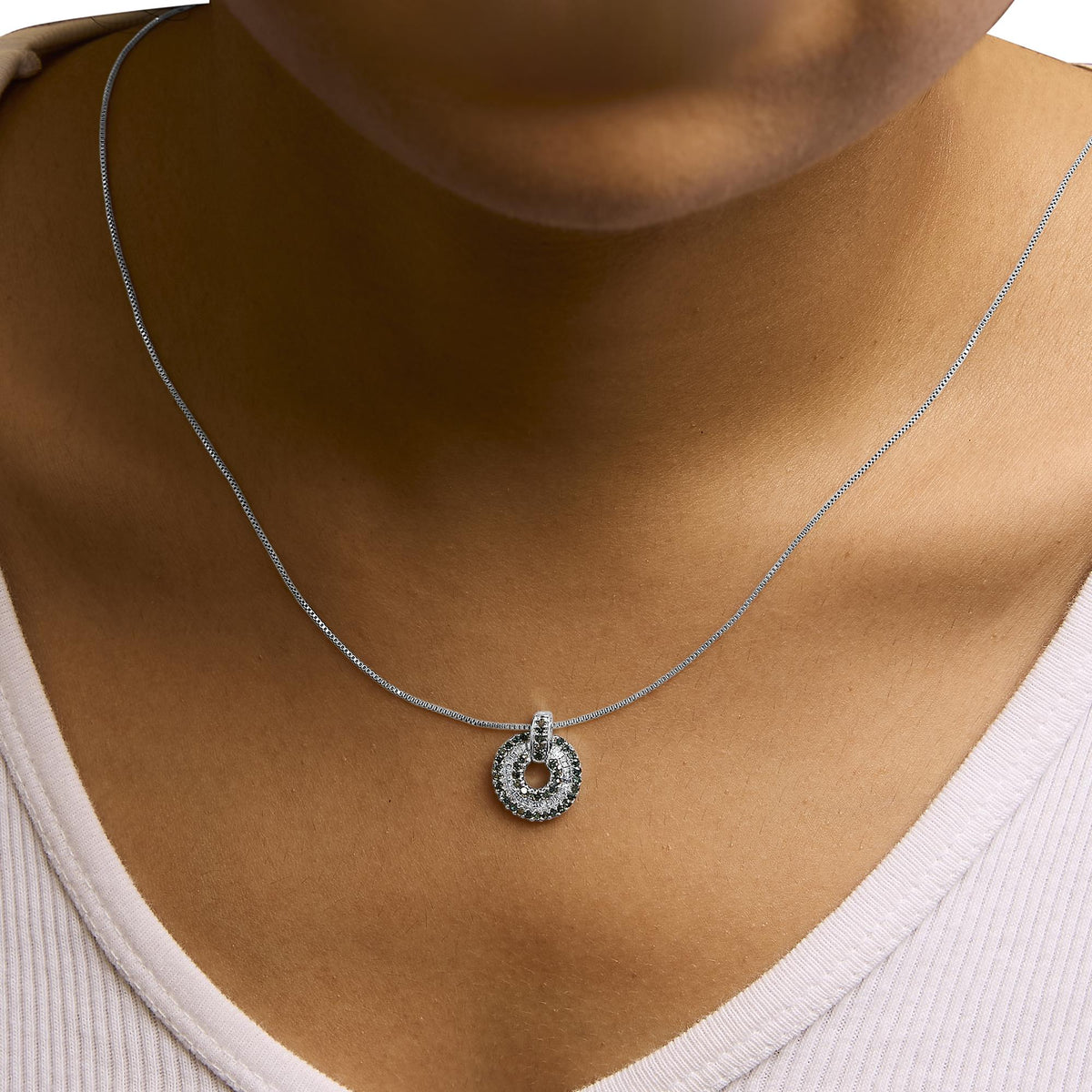 Close-up front view of a model wearing a white metal necklace with a circular pendant featuring round blue gemstones in prong settings and baguette white gemstones in channel settings.