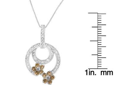White metal necklace pendant with two overlapping circular designs set with round white gemstones, accented by two flower shapes with round champagne gemstones, shown hanging from a chain with a scale for size reference, front-facing angle.