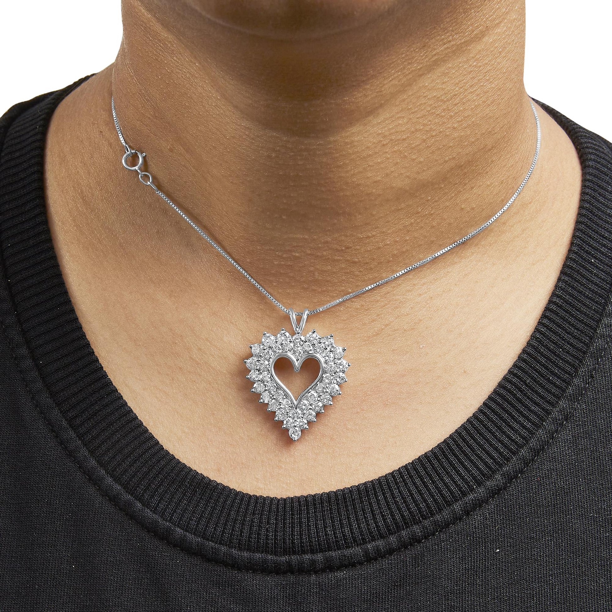 Close-up front view of a white metal heart-shaped pendant necklace with round white gemstones in prong settings surrounding the open heart center, worn on a model.