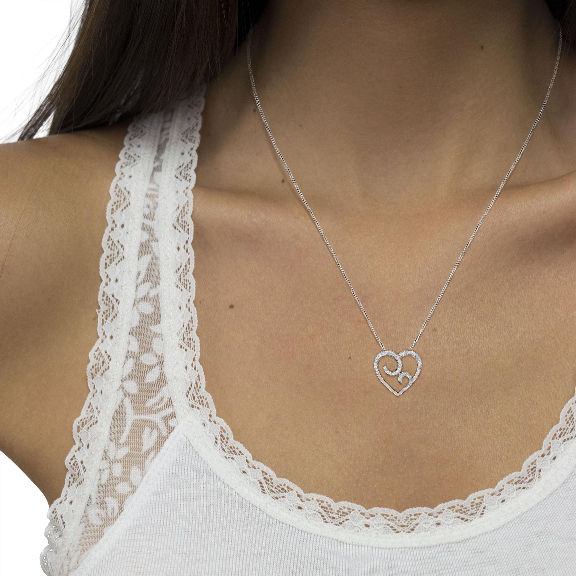 Close-up front view of a white metal necklace with a heart-shaped pendant adorned with round pave-set white gemstones, worn on a model.