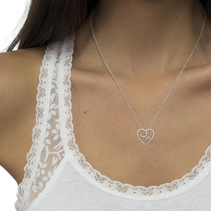Close-up front view of a white metal necklace with a heart-shaped pendant adorned with round pave-set white gemstones, worn on a model.