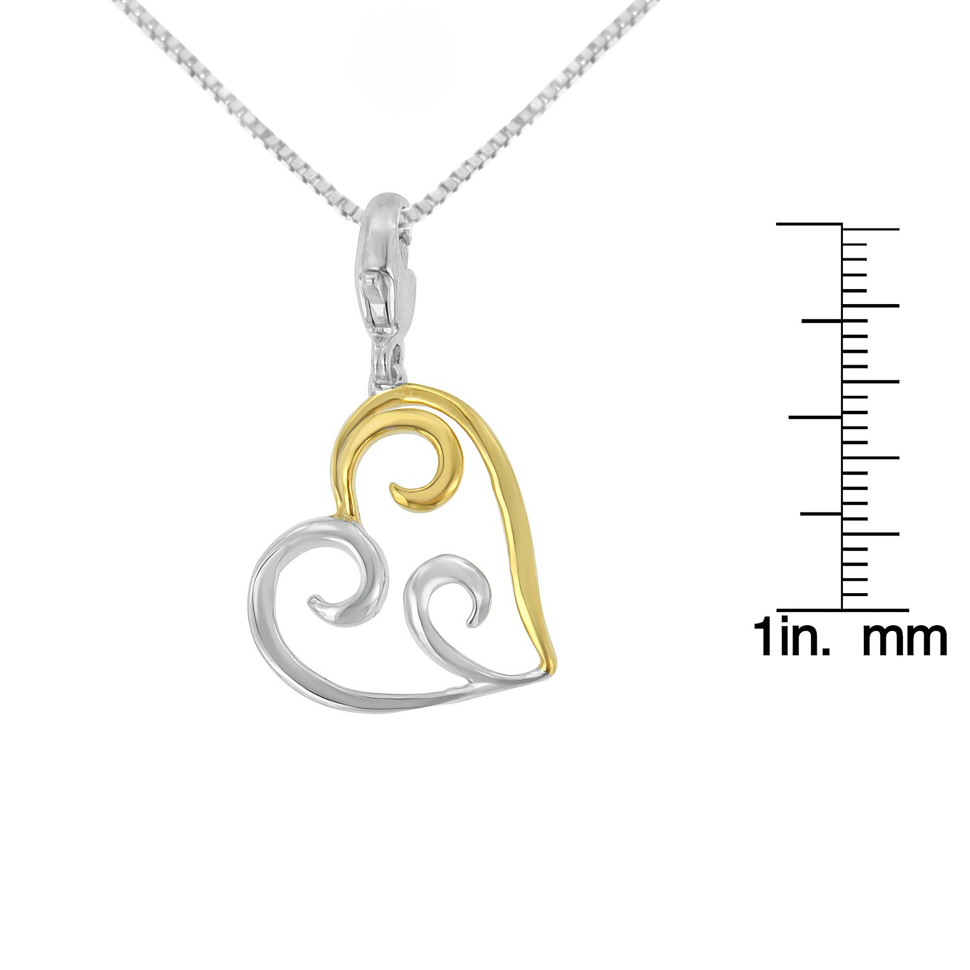 Close-up front view of a heart-shaped necklace pendant with yellow and white metal swirls, shown next to a ruler for size reference.