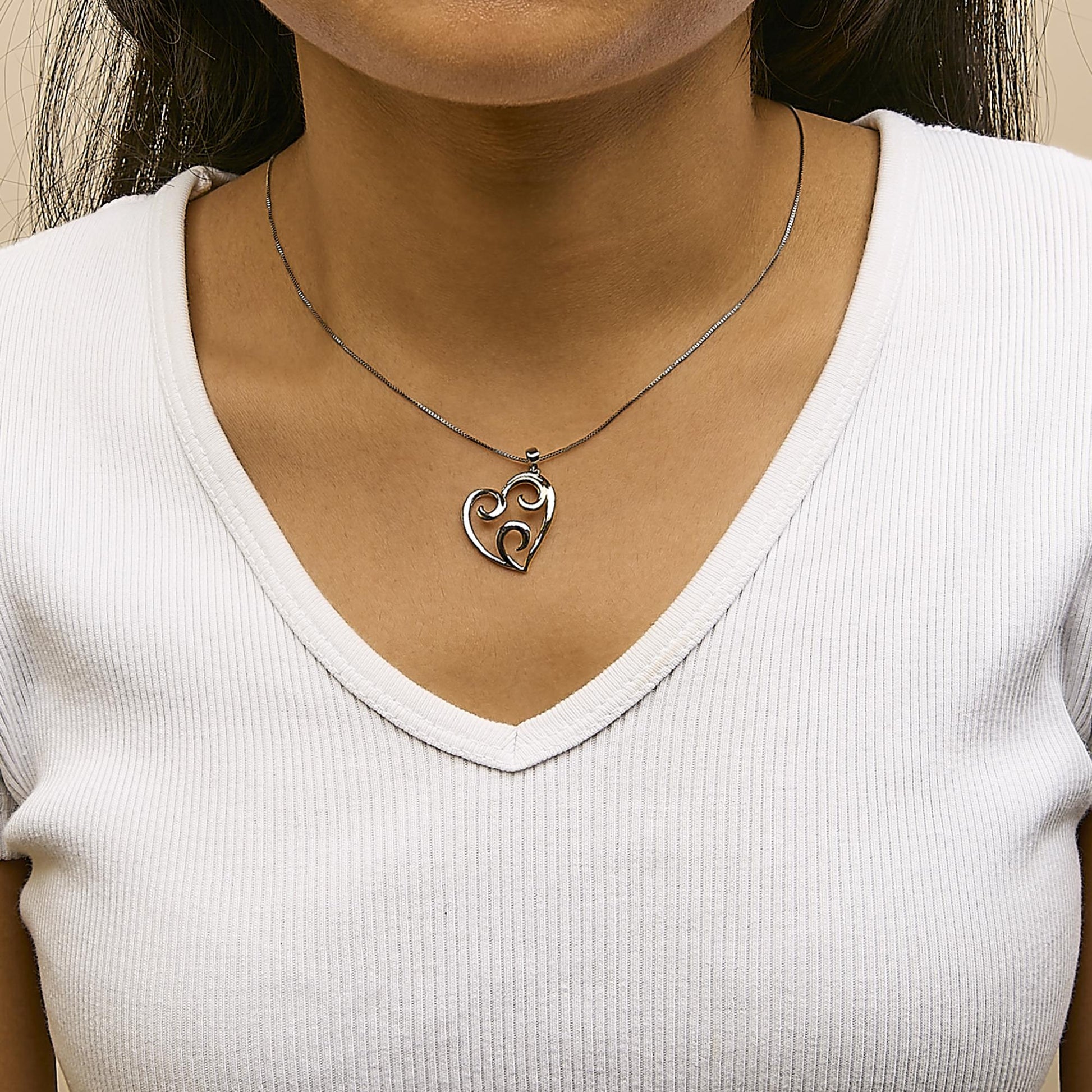 Two-toned heart-shaped necklace pendant with swirl design, shown on a model from a front angle.