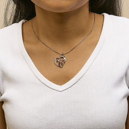Two-toned heart-shaped necklace pendant with swirl design, shown on a model from a front angle.