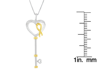 Front view of two-toned key-shaped necklace pendant with heart-shaped top, adorned with small white round prong-set gemstones and a gold-toned ribbon detail, shown next to a ruler for size reference.