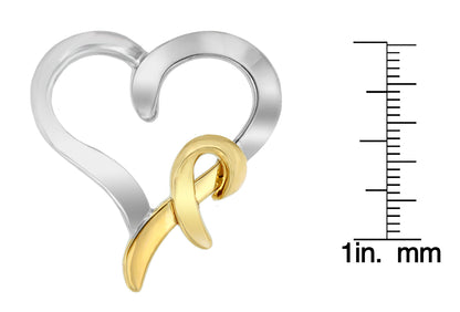 Two-toned heart-shaped necklace pendant with a ribbon detail, shown from a front angle, placed next to a ruler for size reference.