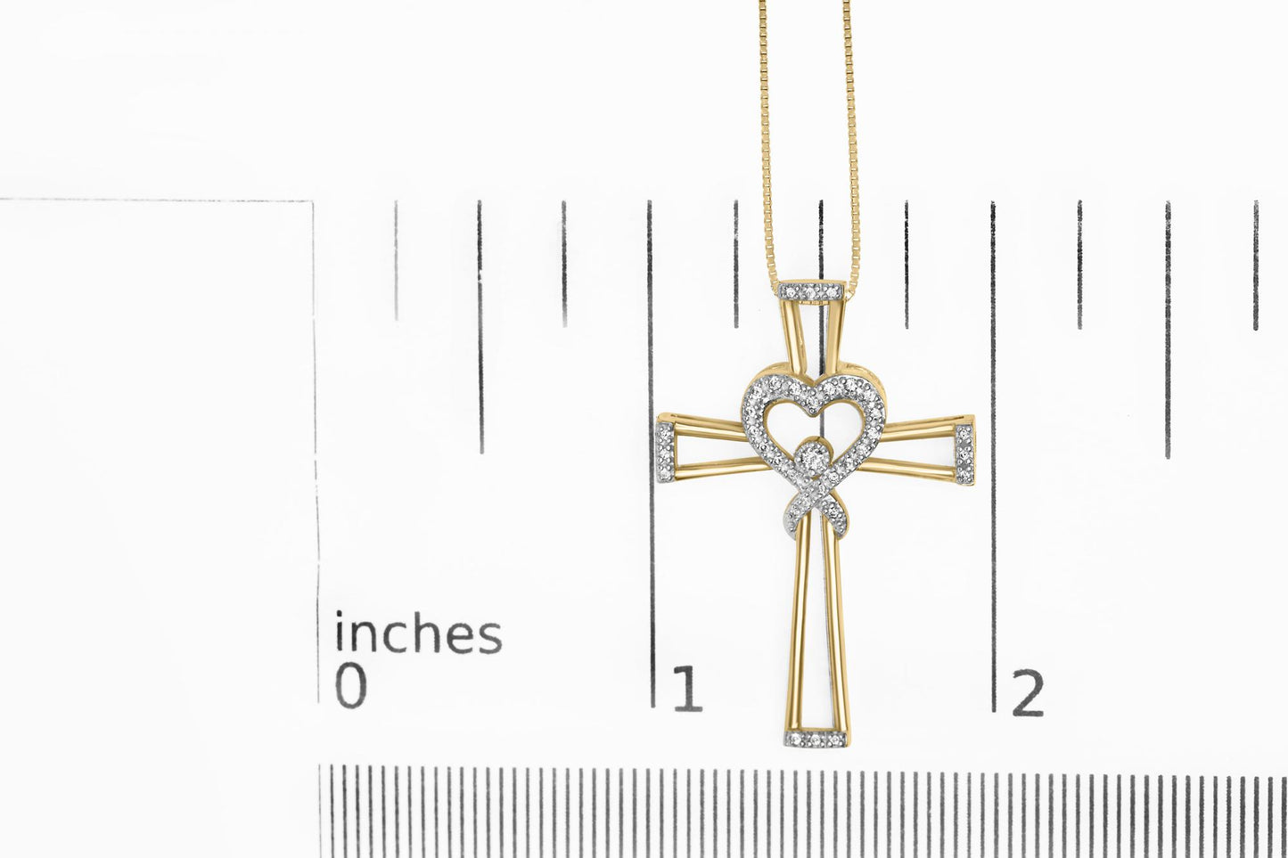 Yellow metal cross necklace with heart and round white gemstones in prong settings, shown flat on a ruler for size reference, top-down angle.