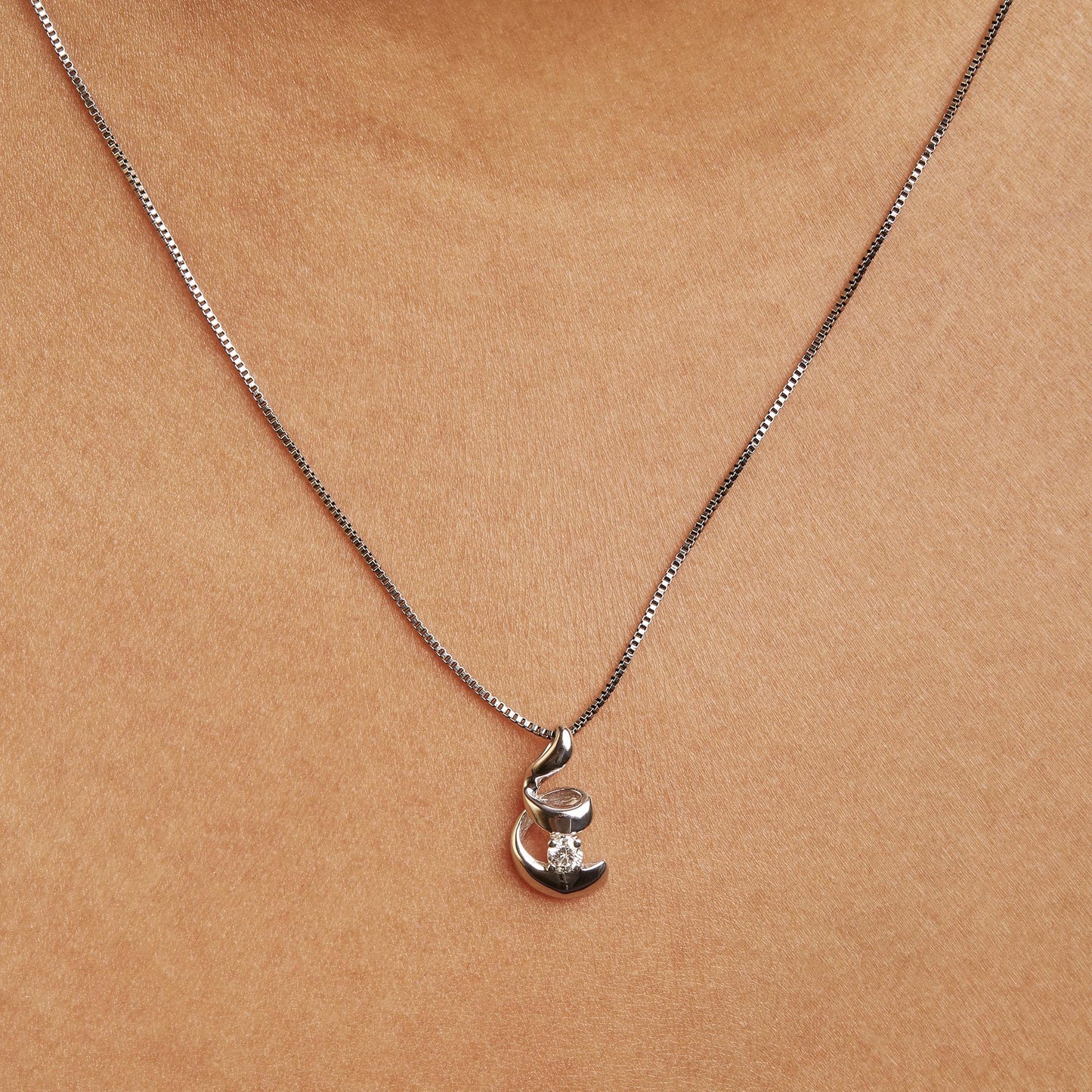 Close-up front view of a white necklace on a model featuring a pendant with a round white gemstone in a 4-prong setting.