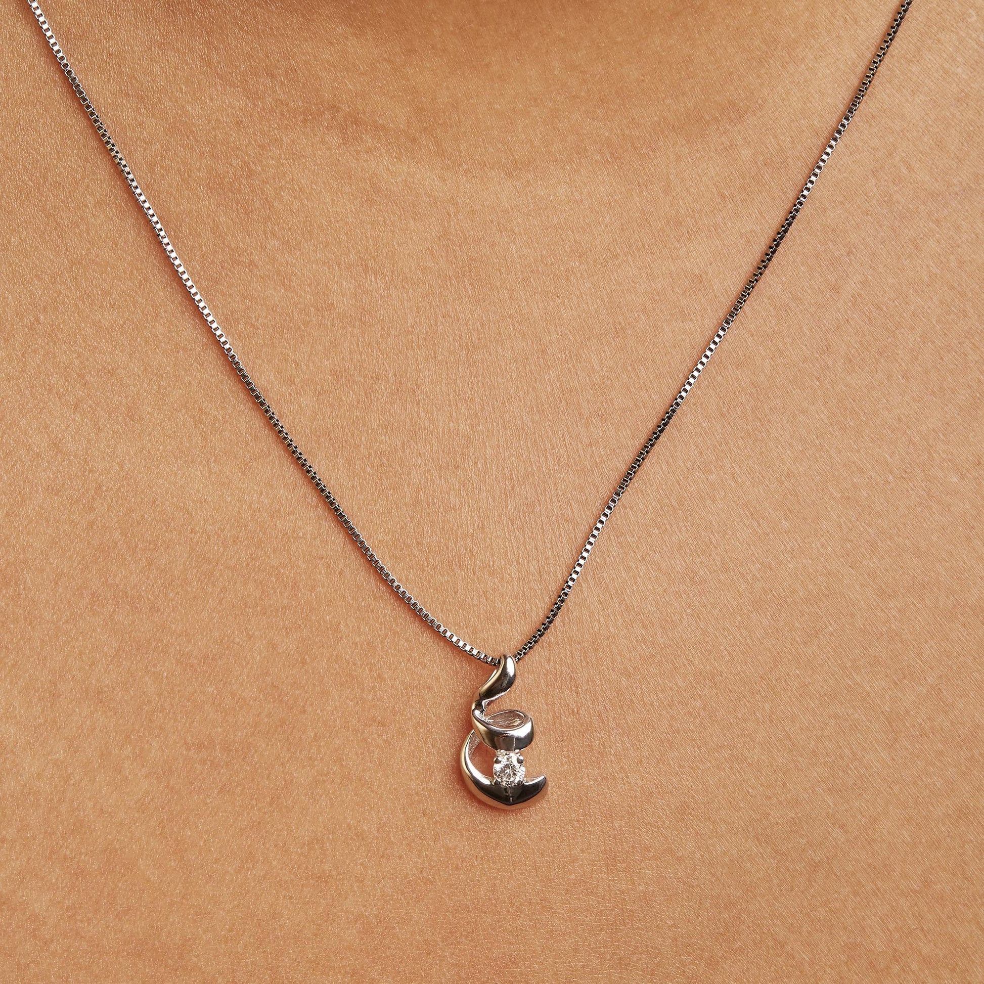 Close-up front view of a white necklace on a model featuring a pendant with a round white gemstone in a 4-prong setting.
