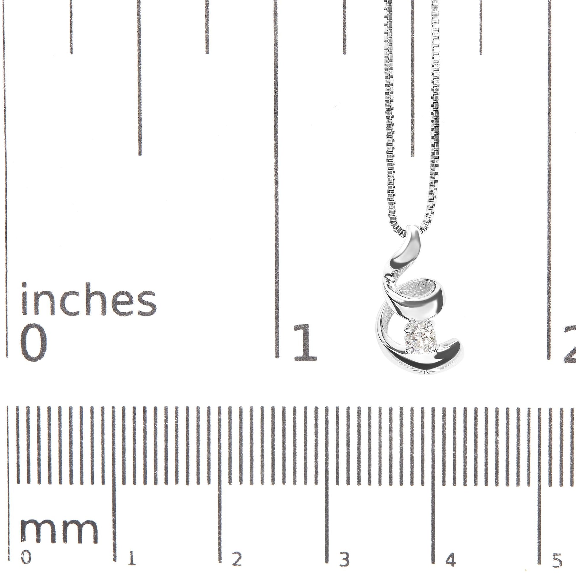 Close-up of a white metal necklace with a curved abstract pendant holding a round white gemstone, displayed on a ruler for size reference.