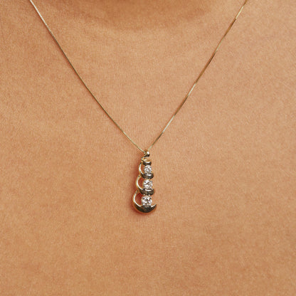 Close-up front view of a yellow necklace pendant featuring three round white gemstones in prong settings, shown worn on a model.