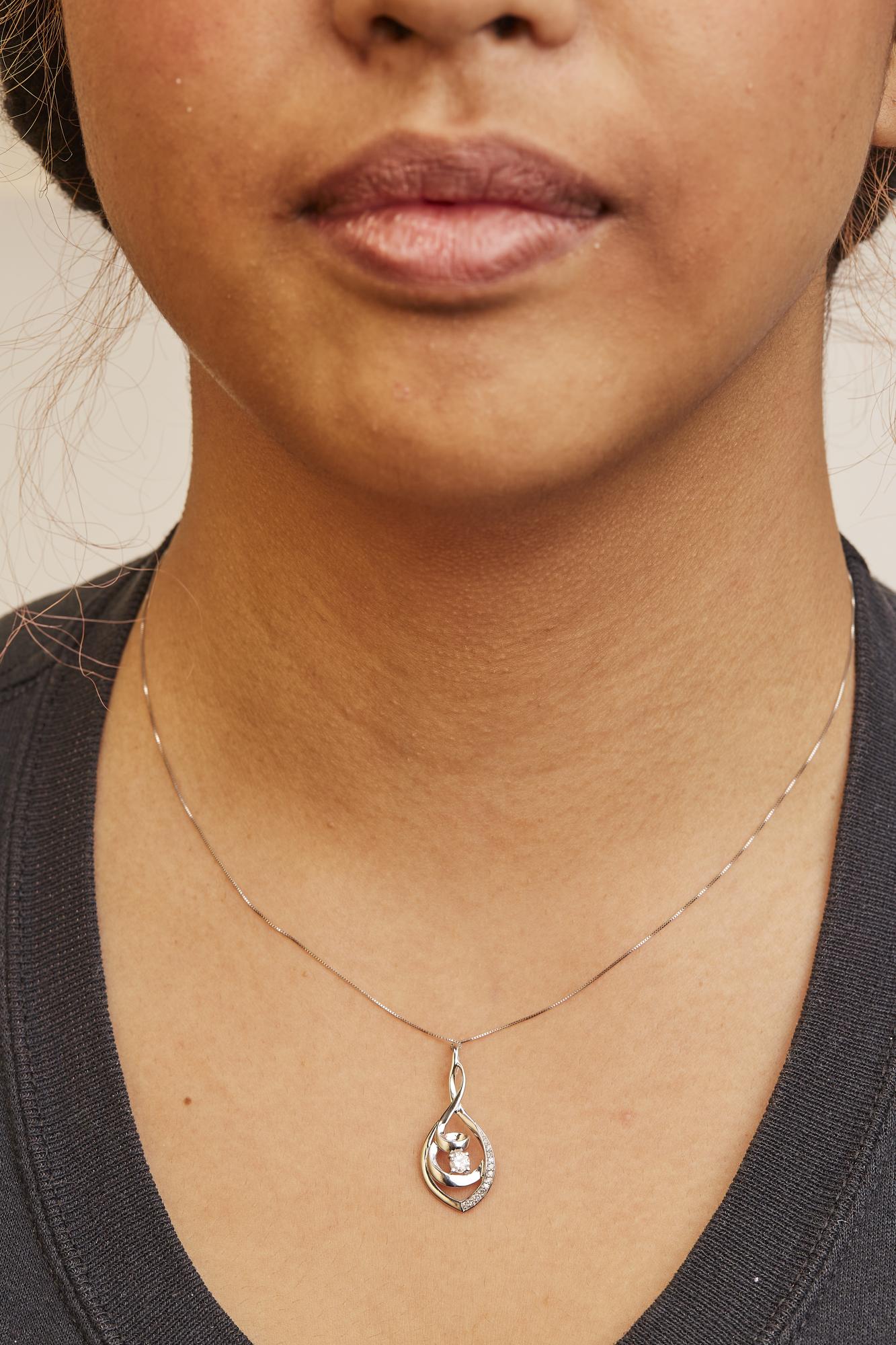 Close-up front view of a model wearing a white metal necklace with a teardrop-shaped pendant featuring a combination of round white gemstones in prong settings.