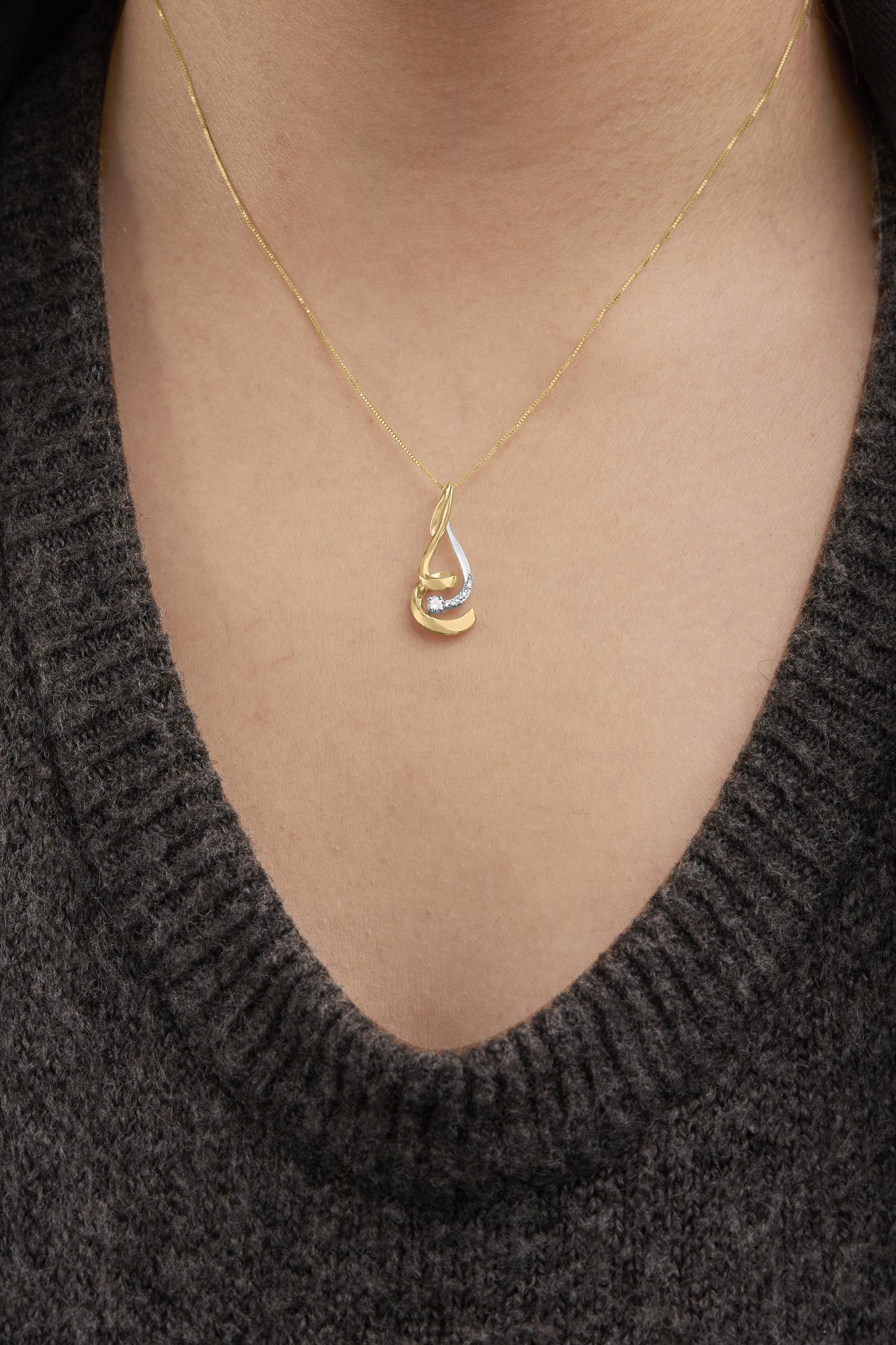 Close-up front view of a two-toned necklace with a teardrop-shaped pendant featuring round white gemstones in prong settings, worn on a model.