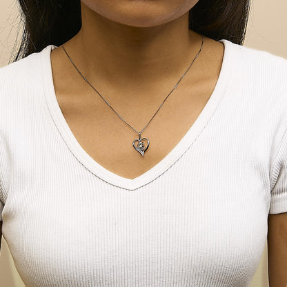Close-up front view of a white metal heart-shaped necklace pendant with a single round white gemstone in prong setting, worn on a model wearing a white ribbed V-neck shirt.