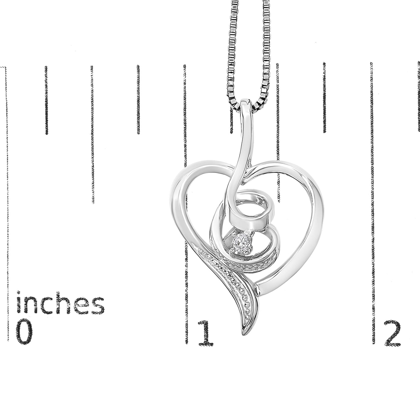 Close-up front view of a white metal heart-shaped necklace pendant with a single round white gemstone, shown on a ruler for size reference.