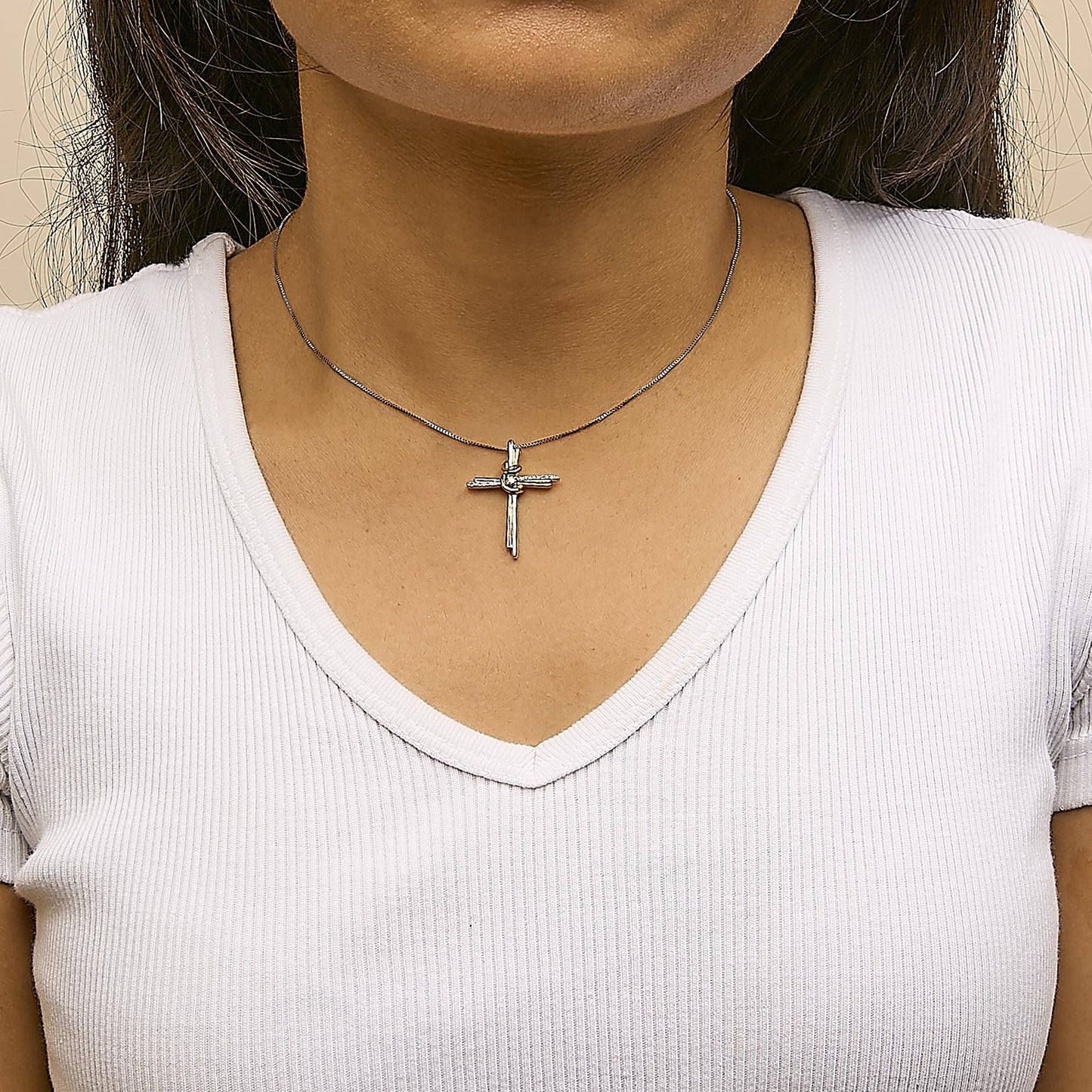 Close-up front view of a two-toned necklace with a cross pendant featuring one larger white gemstone and multiple smaller white gemstones, worn on a model with a white top.