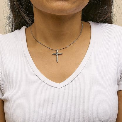 Close-up front view of a two-toned necklace with a cross pendant featuring one larger white gemstone and multiple smaller white gemstones, worn on a model with a white top.