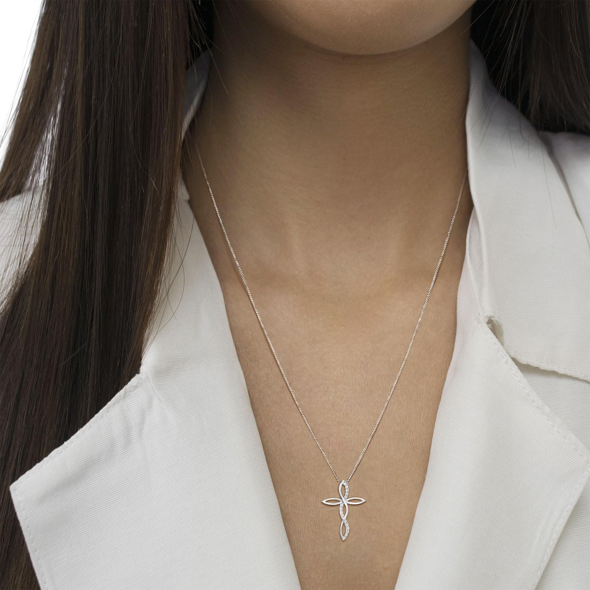 White metal necklace with a cross pendant featuring round white gemstones in prong settings, worn on a model, front-facing close-up shot.