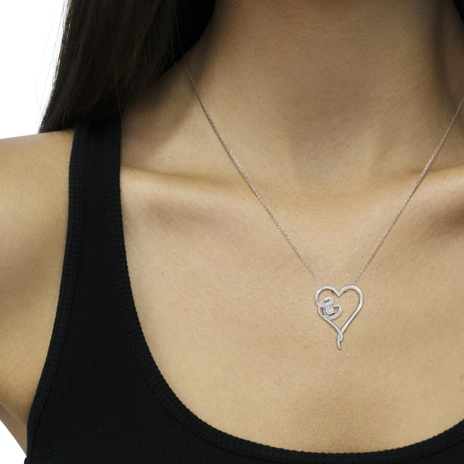 Close-up front view of a white metal heart-shaped necklace with a delicate chain, featuring a small cluster of white gemstones on one side, worn on a model with a black top.