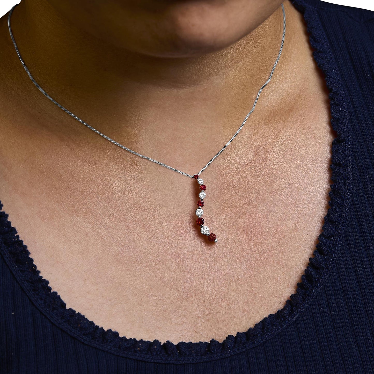 Close-up front angle of a white metal necklace on a model with a vertical pendant featuring alternating round-shaped red and white gemstones in shared prong settings.