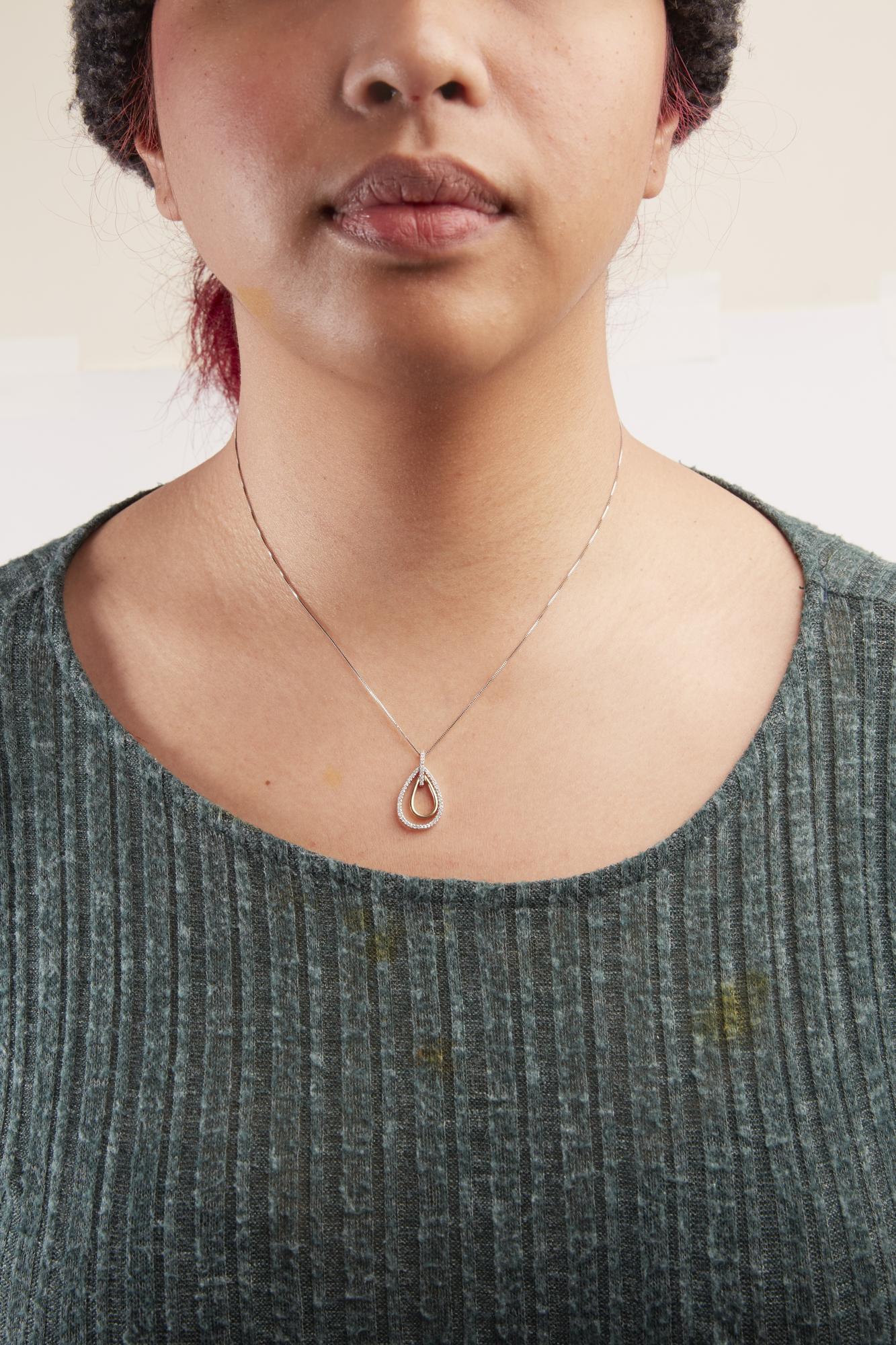 Two-toned necklace with teardrop-shaped pendant featuring round white gemstones in prong setting, worn on a model, front-facing angle.