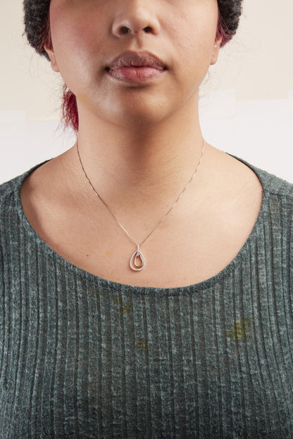 Two-toned necklace with teardrop-shaped pendant featuring round white gemstones in prong setting, worn on a model, front-facing angle.