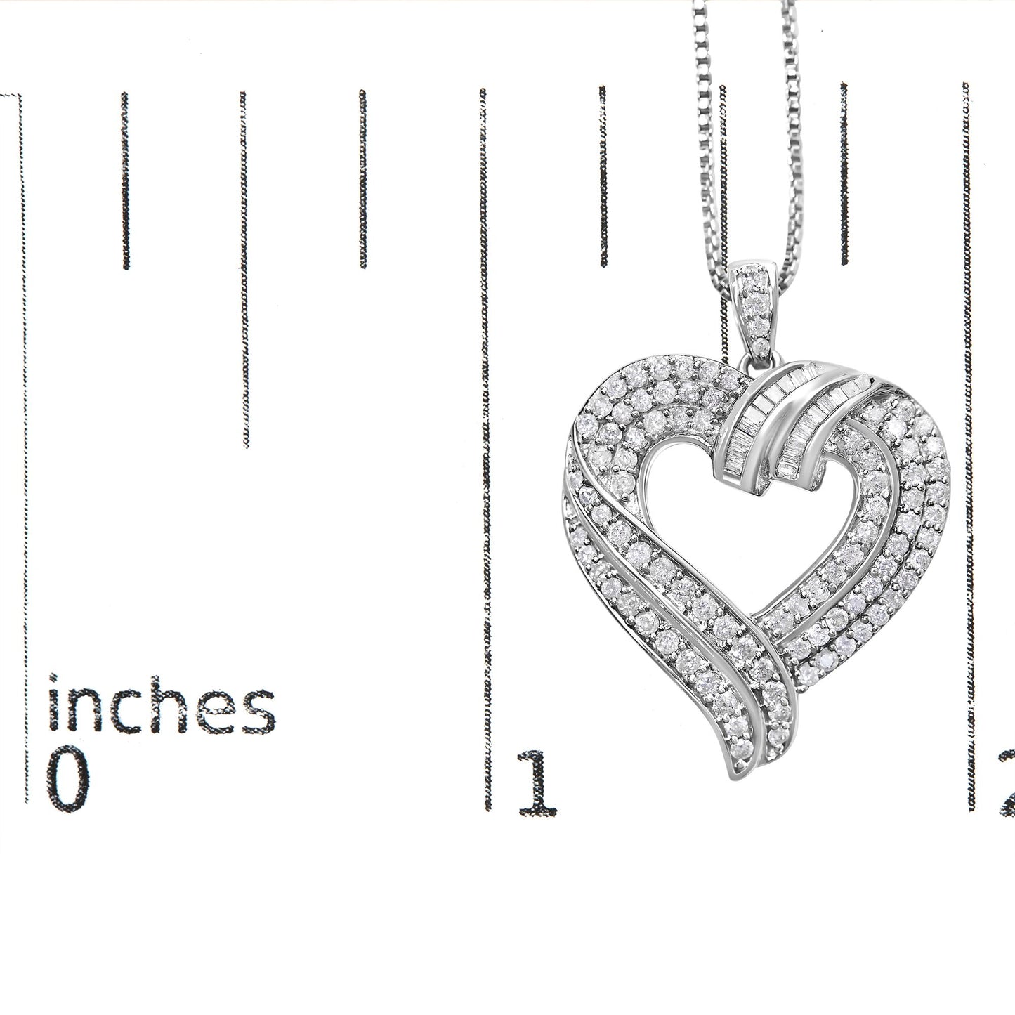 Close-up front view of a white metal heart-shaped necklace pendant with round white gemstones in prong settings and baguette white gemstones in channel settings, shown on a ruler for size reference.