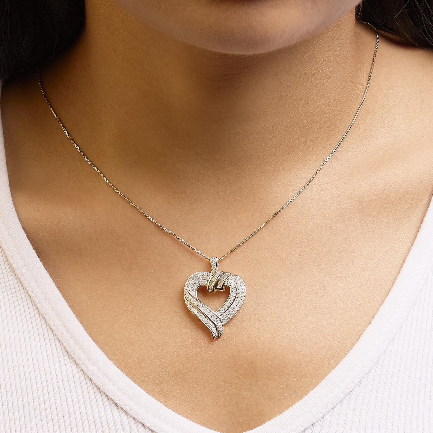 Close-up front view of yellow necklace on a model featuring a heart-shaped pendant adorned with white round prong-set gemstones and white baguette channel-set gemstones.