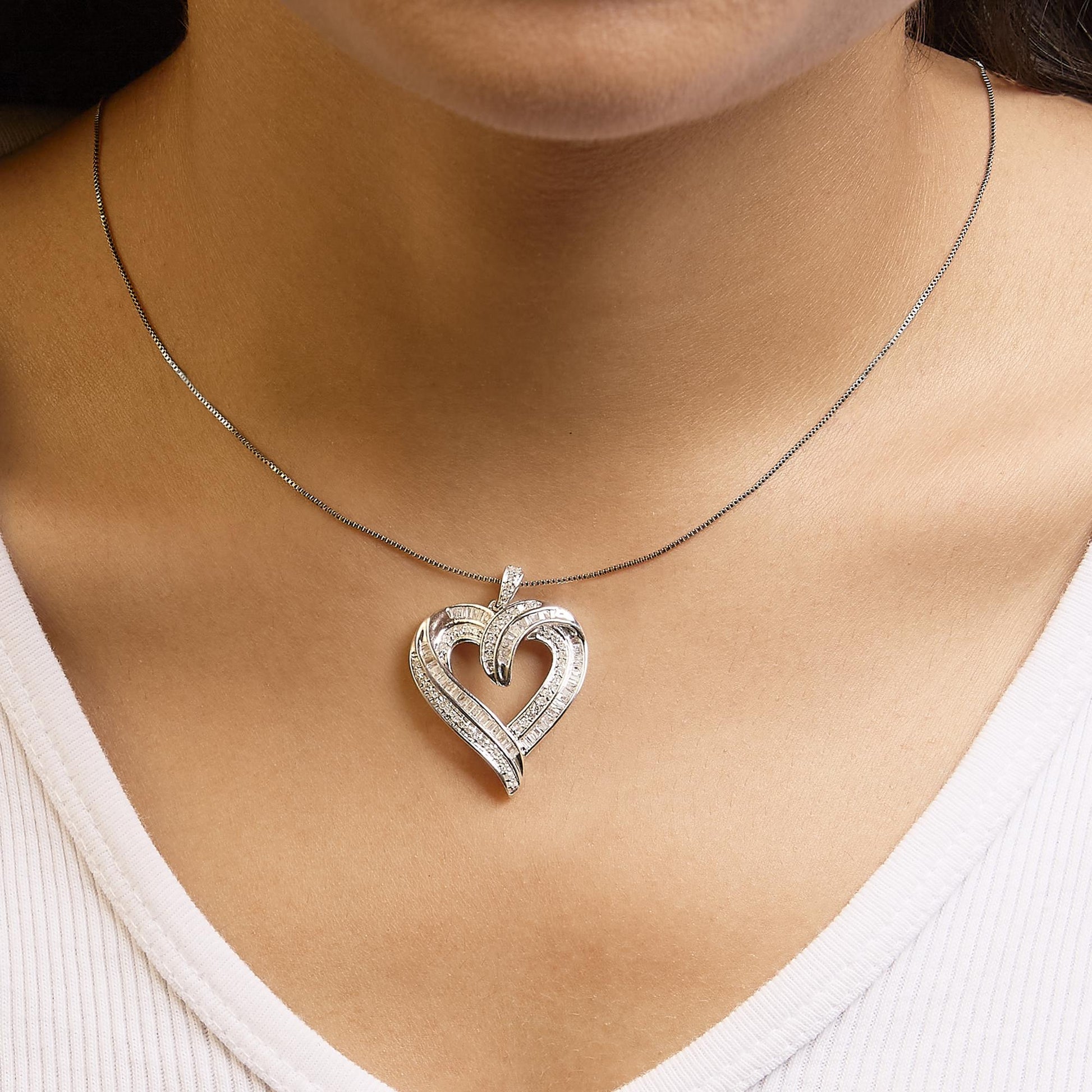 Close-up front view of a white metal heart-shaped necklace pendant with round prong-set white gemstones and baguette channel-set white gemstones, worn on a model.