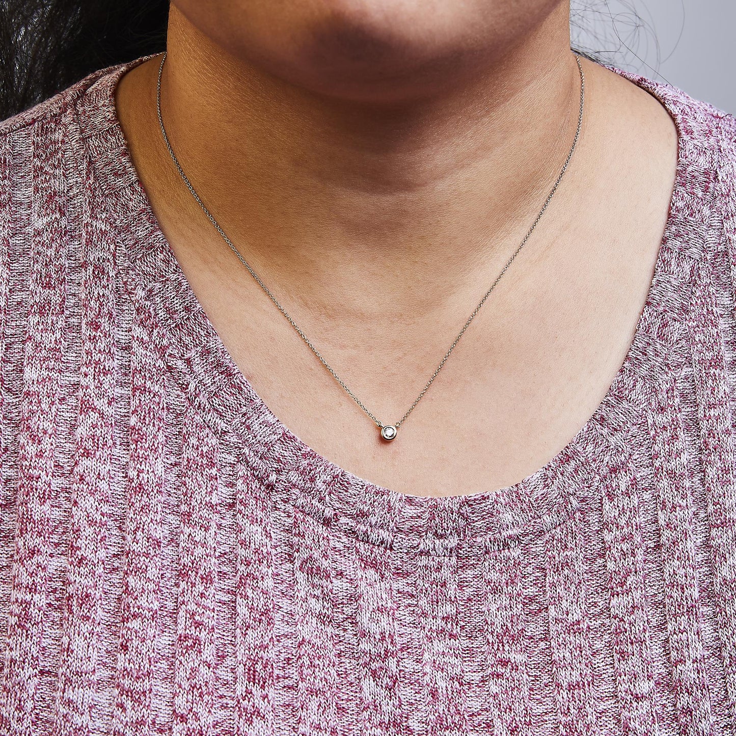 Close-up front view of a rose metal necklace with a single round white gemstone in a bezel setting, worn on a model.