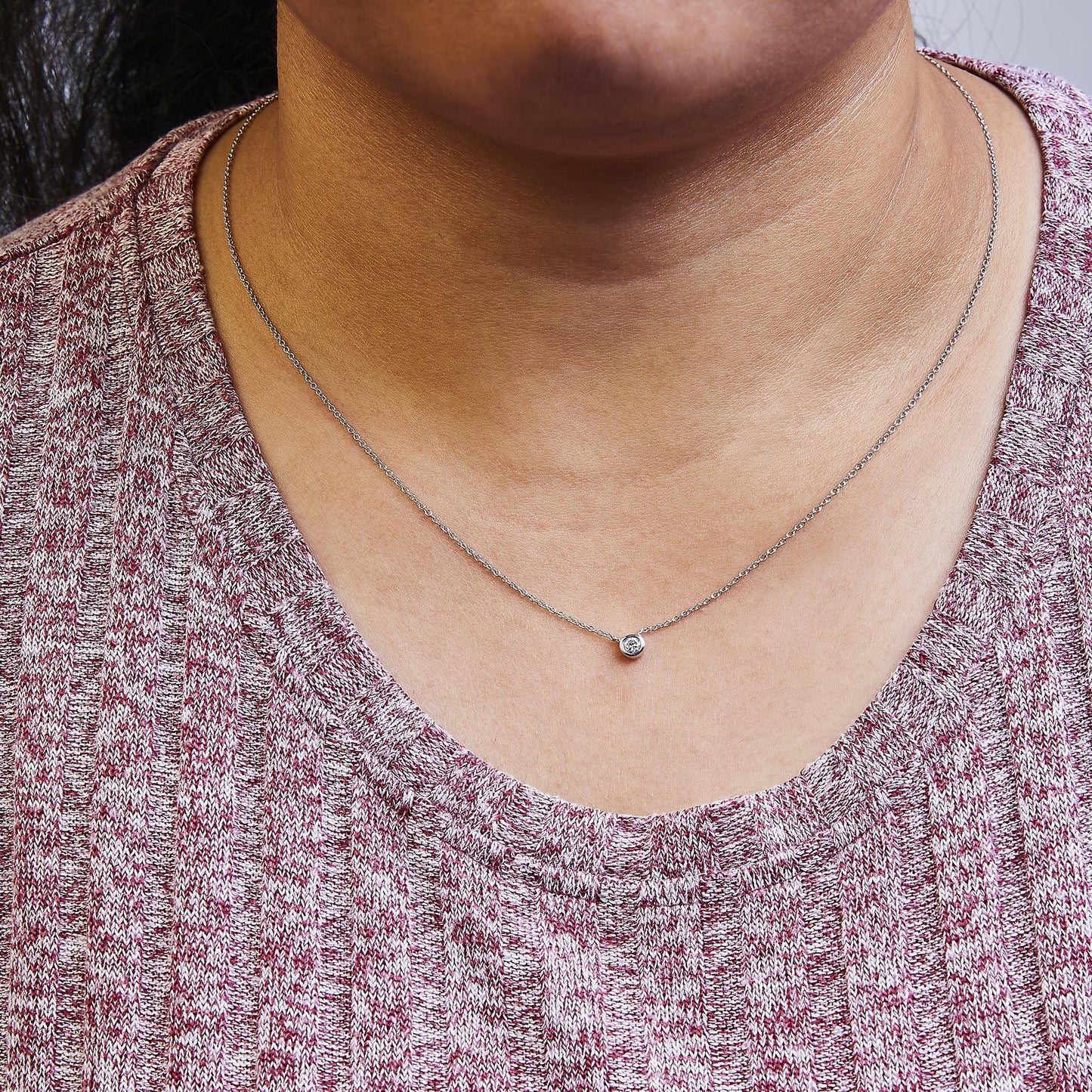 Close-up front view of a white metal necklace with a single round white gemstone in bezel setting, worn on a model.