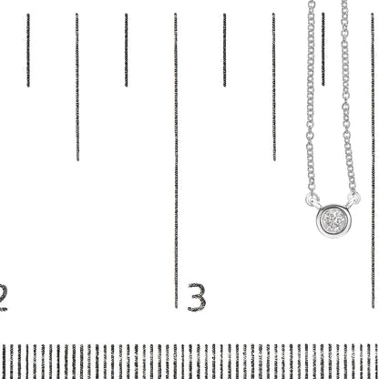 Close-up front angle of a white metal necklace with a single round bezel-set white gemstone pendant, displayed on a ruler for size reference.