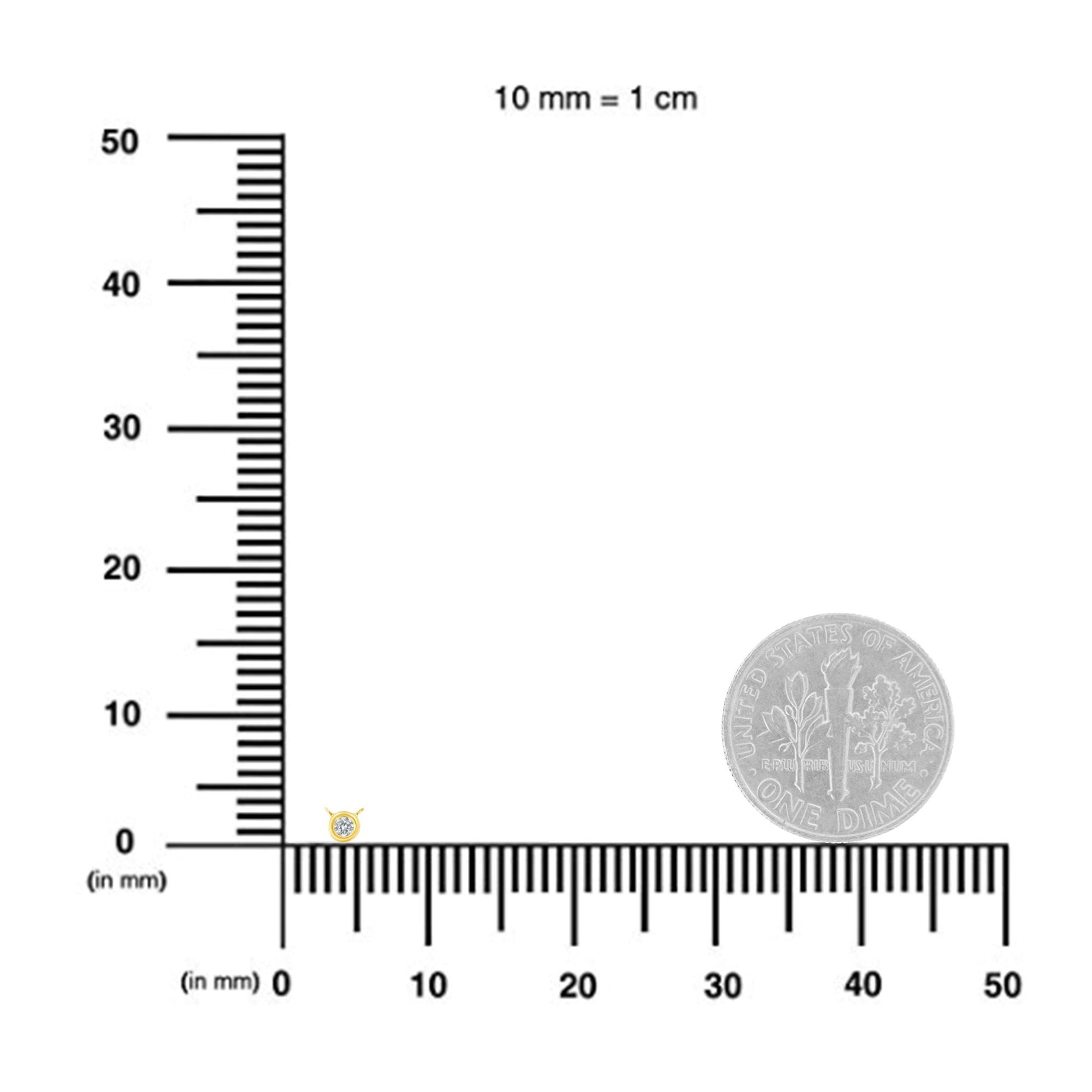 Close-up view of a yellow metal necklace pendant with a single round white gemstone in bezel setting, displayed on a ruler for size reference.