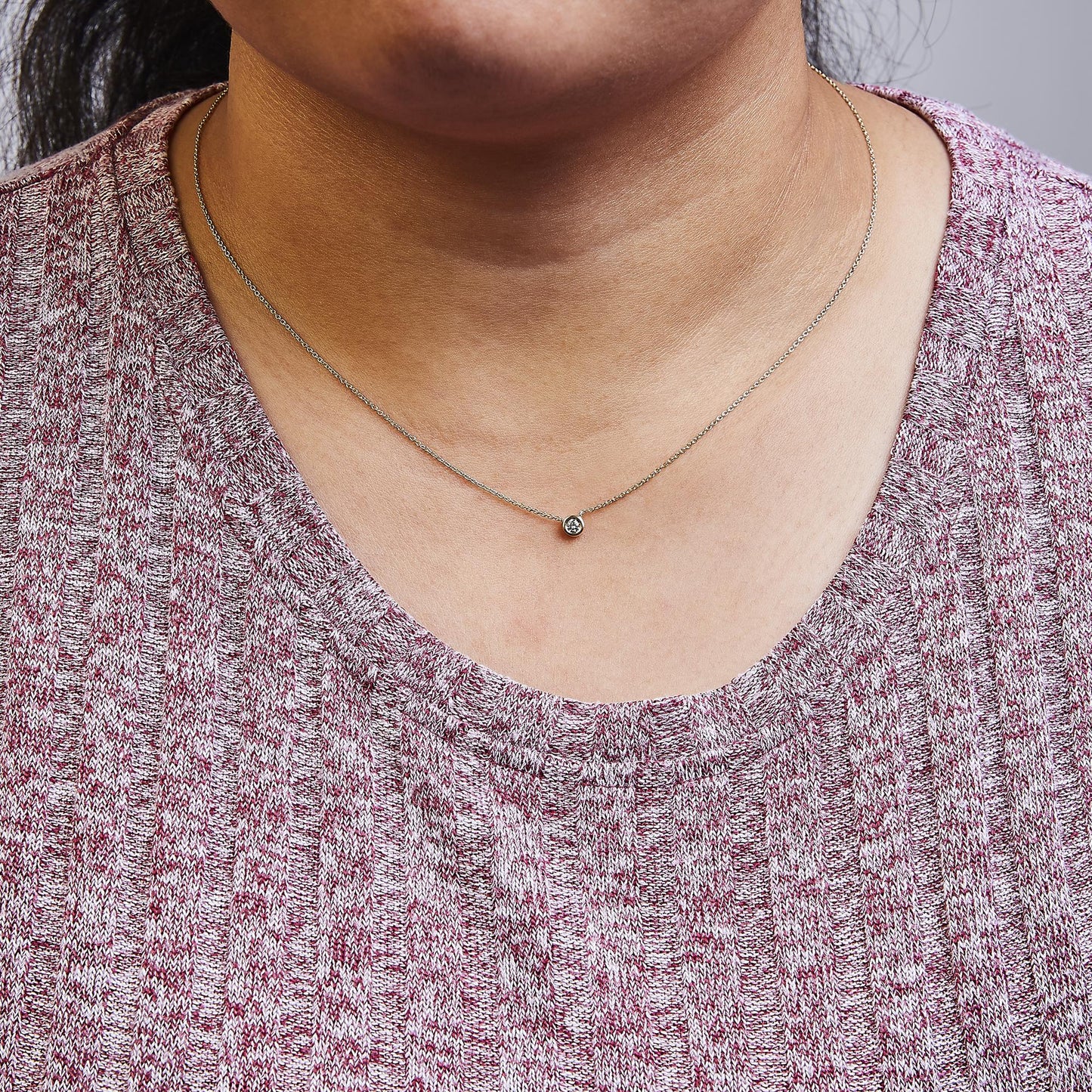Close-up front view of a model wearing a yellow metal necklace with a single round white gemstone in a bezel setting.