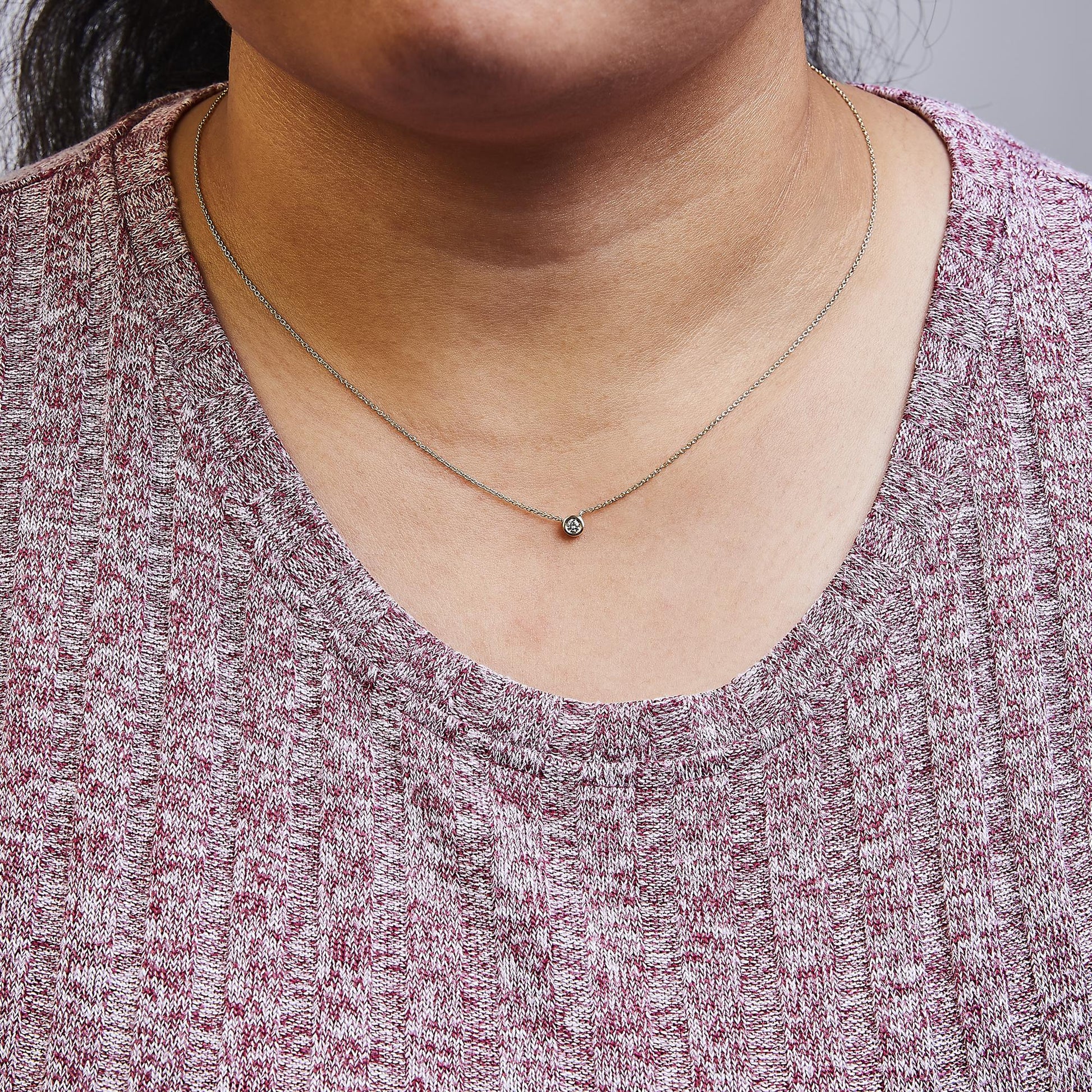 Close-up front view of a model wearing a yellow metal necklace with a single round white gemstone in a bezel setting.