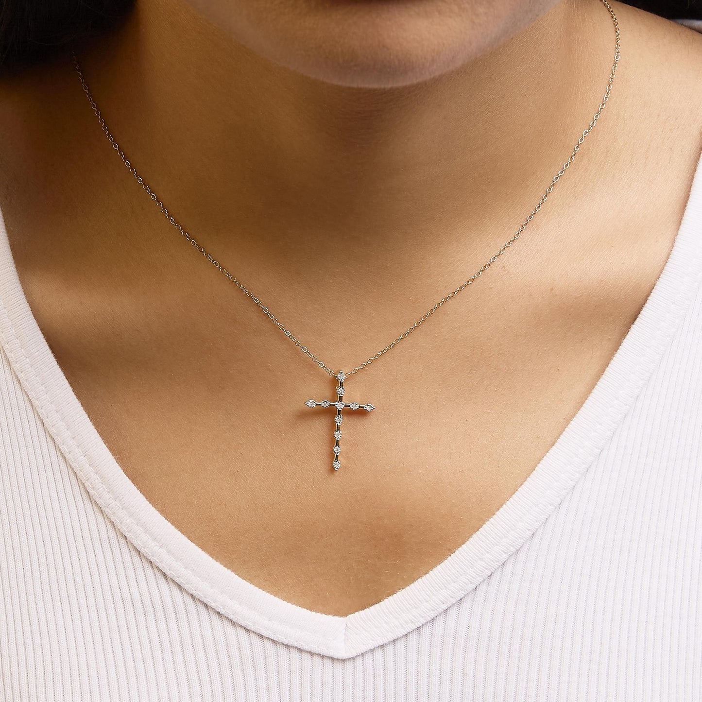 Close-up shot of a yellow metal necklace on a model, featuring a cross pendant set with round white gemstones in a miracle setting.