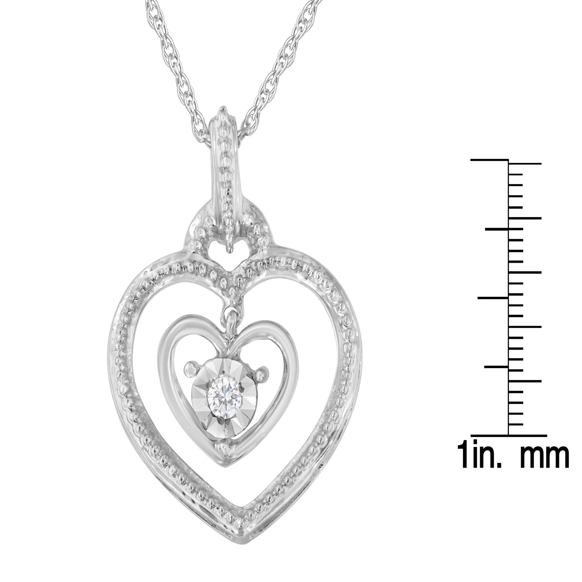 Front angle of white metal heart-shaped necklace pendant with an inner heart featuring a single round white gemstone, shown next to a ruler for size reference.