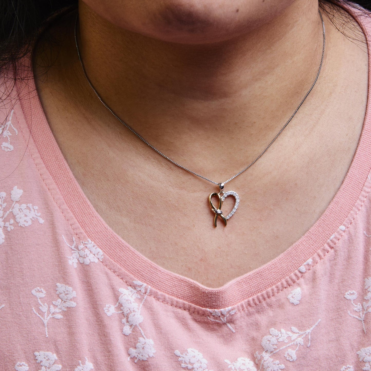 Necklace on model showing a pendant with a heart shape featuring yellow and white metal and white round gemstones on a chain, front-facing angle.