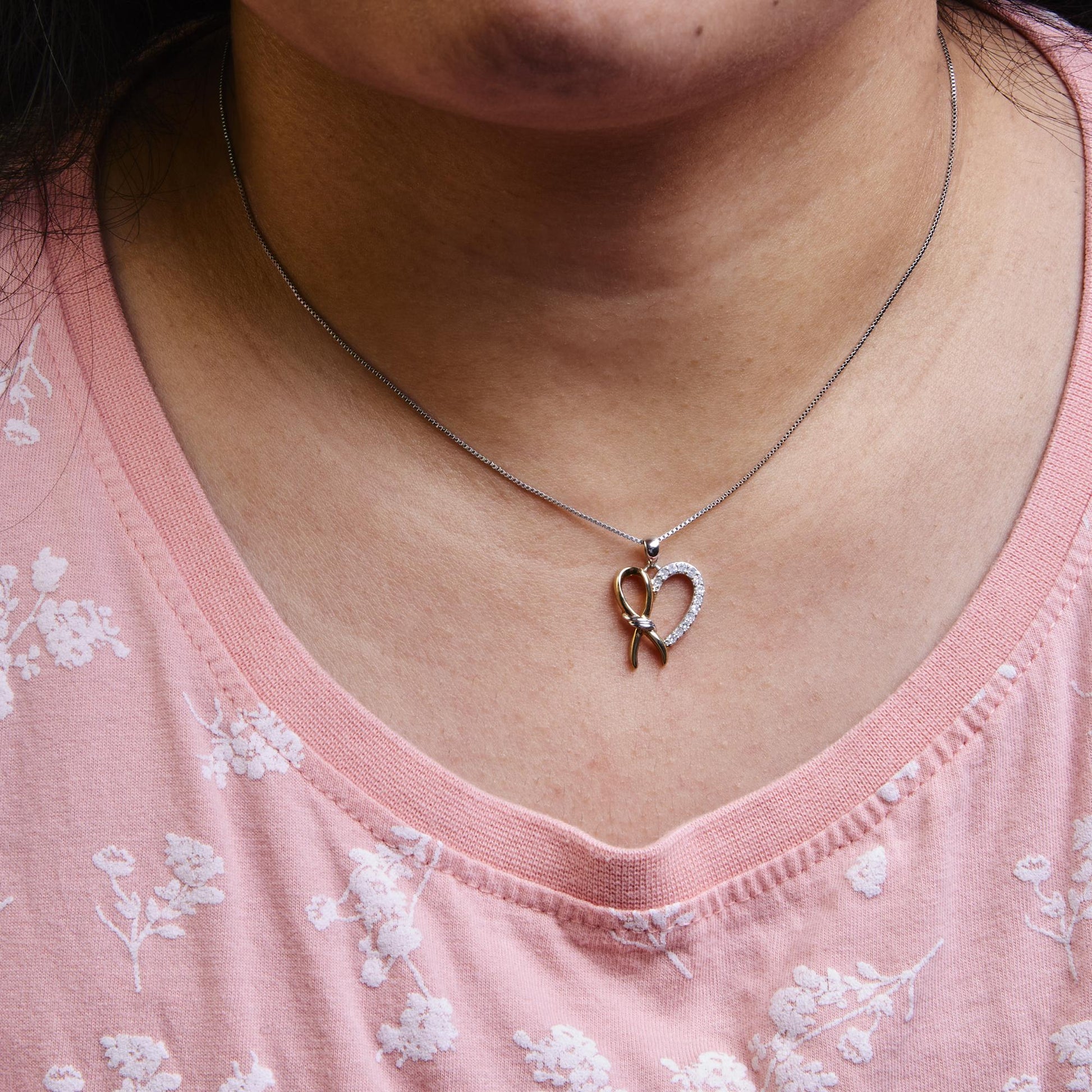 Necklace on model showing a pendant with a heart shape featuring yellow and white metal and white round gemstones on a chain, front-facing angle.