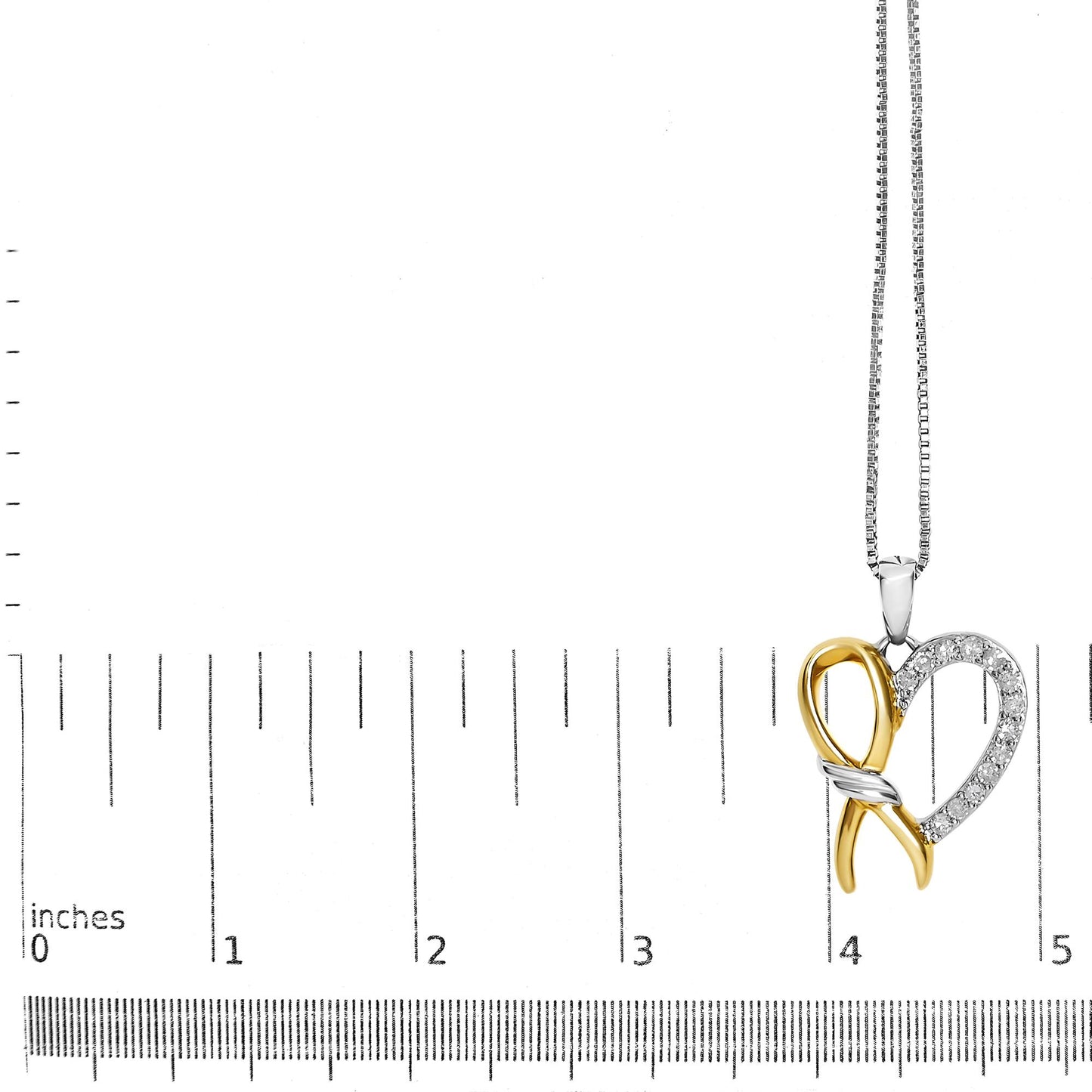 Close-up front angle of a two-tone yellow and white metal heart-shaped necklace pendant with white round prong-set gemstones, displayed on a ruler for size reference.