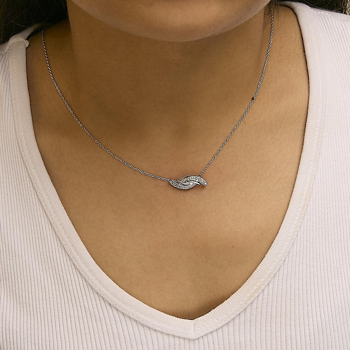 Close-up front view of a model wearing a white metal necklace with a curved pendant set with round white gemstones in a prong setting.