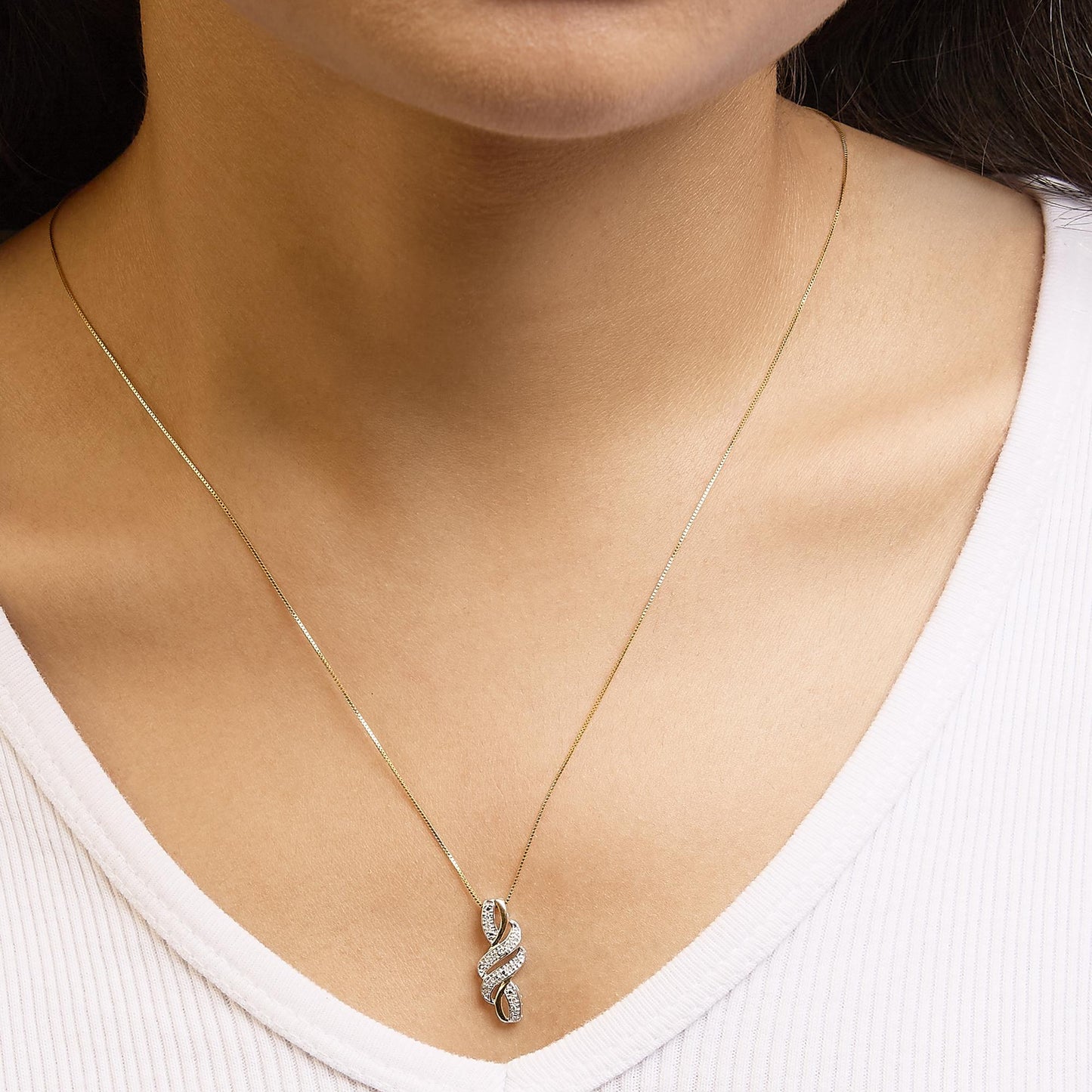 Close-up front view of a yellow metal necklace with a pendant featuring intertwined design adorned with white round gemstones in pave setting, worn on a model.