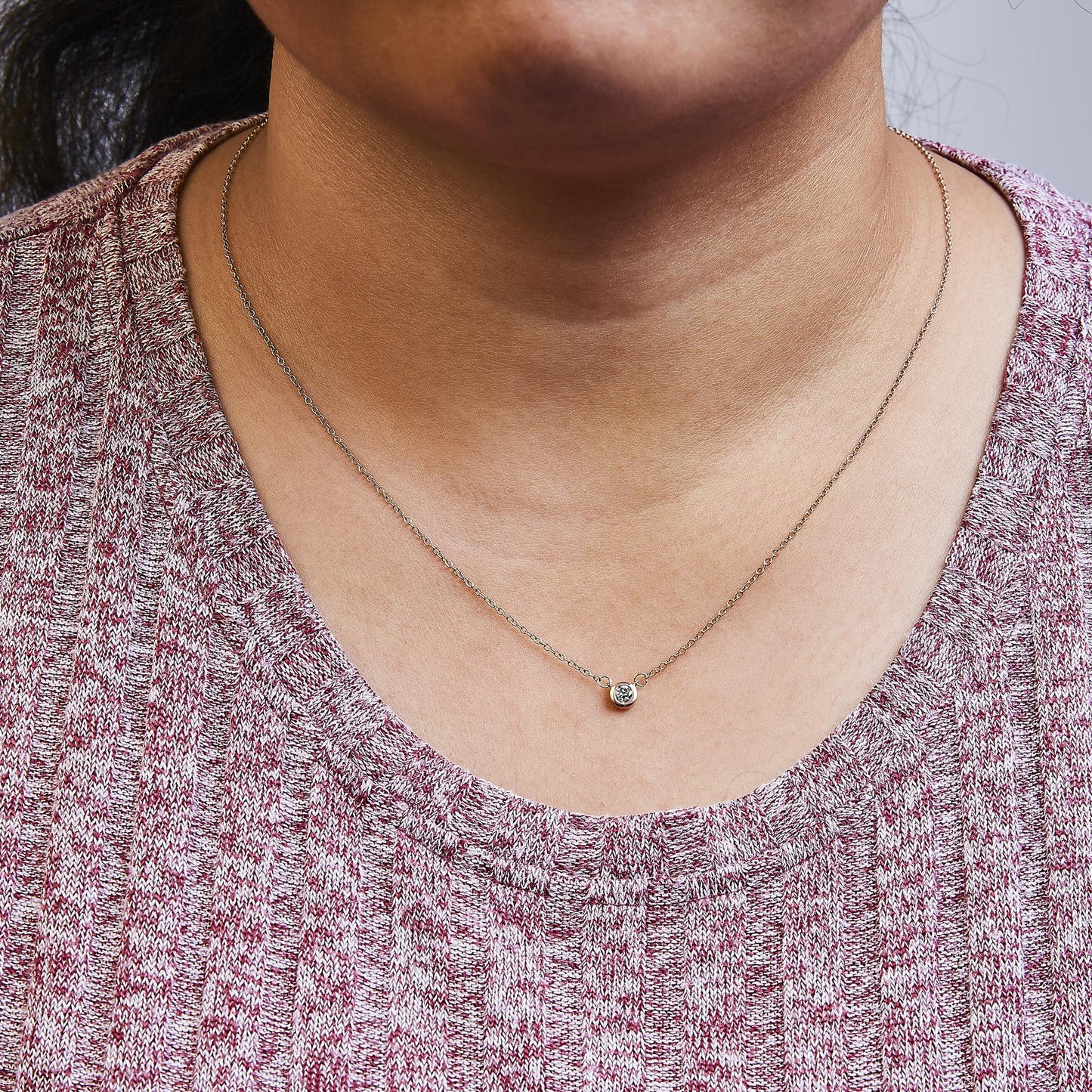 Close-up front view of a rose metal necklace with a round white gemstone in bezel setting, worn on a model.