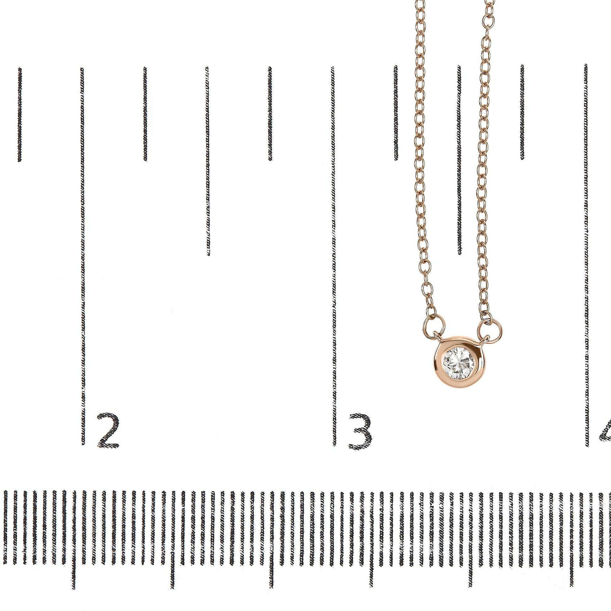 Close-up front view of a rose metal necklace with a round white gemstone in bezel setting, displayed on a ruler for size reference.