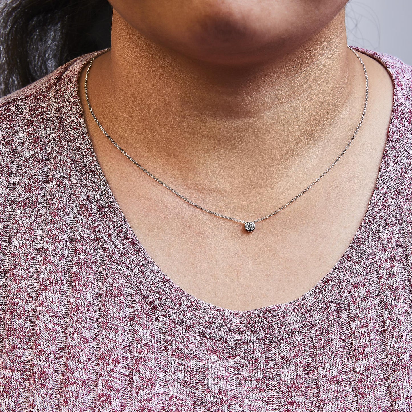 Close-up front view of a white metal necklace with a round white gemstone in bezel setting worn on a model.